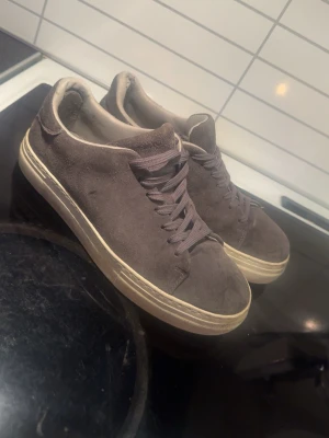 Grå mockasneakers med vit sula - Stilrena sneakers i grå mocka med matchande grå skosnören och vit, något tjockare sula. Klassisk låg modell som passar till det mesta och ger en clean look. 