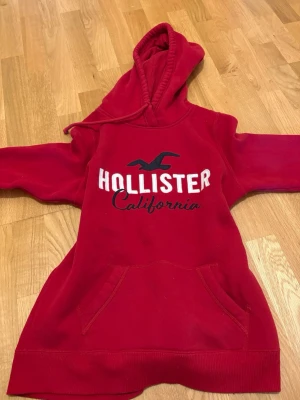 Röd Hollister hoodie med tryck - Säljer den här jättesnygga röda hoodien från Hollister med broderat tryck 'Hollister California' på bröstet.  Storlek s och passar bra i storleken.