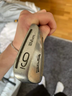 Wilson Reflex golfklubba 9a - Golfklubba från Wilson, modell Reflex, i silverfärgad metall. Klubban har svart text och detaljer, samt ett grepp i mörkgrönt. Perfekt för dig som vill testa golf eller behöver en extra klubba till samlingen. En 9a