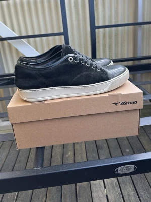 Lanvin - Snygga svarta sneakers från lanvin i mocka med vita sulor och metallfärgade öljetter. Klassisk låg modell med snörning och stilren design som passar till det mesta. Perfekta för dig som gillar en clean och enkel look. Priset är intw hugget i sten