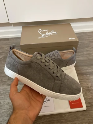 Christian Louboutin skor - Snygga gråa sneakers från Christian Louboutin i mocka med vita sulor och matchande grå skosnören. Klassisk låg modell med diskret design och exklusiv känsla. Perfekta för dig som gillar stilrena och lyxiga skor.
