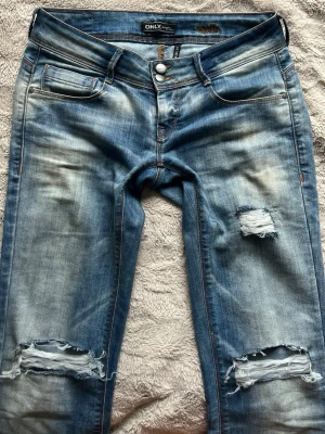 Lågmidjade bootcut slitna jeans - Säljer ett par blåa slitna jeans från only, köptes begangnat men är i väldigt bra skick. Är i strlk 34 och passae längd 170, skriv för fler bilder, mått eller prisförslag💕💕