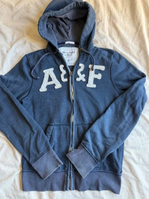 Blå hoodie från Abercrombie & Fitch - Snygg blå hoodie med dragkedja från Abercrombie & Fitch. Sitter väldigt skönt och är perfekt nu till sommaren. Vid frågor eller funderingar är det bara att höra av sig!