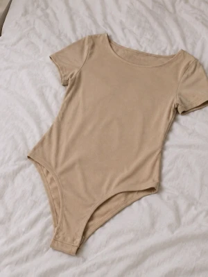 Beige ribbad body med kort ärm - Snygg beige body i ribbat material med korta ärmar och rund halsringning. Praktisk knäppning med tryckknappar i grenen för enkel på- och avtagning. Perfekt att styla till jeans eller kjol för en clean look.