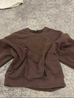 Brun  hoodie - Mysig brun  hoodie med rund hals och breda muddar vid ärmslut och nederkant. Tillverkad i mjukt bomullsmaterial som ger en avslappnad och trendig look. Perfekt för dig som gillar en enkel och stilren stil.