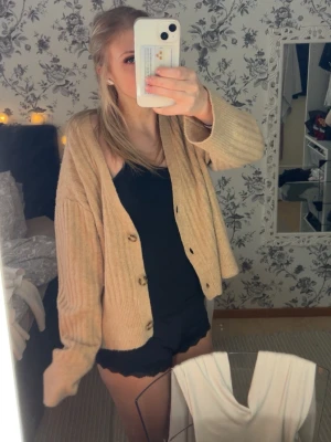 Beige ribbstickad kofta med knappar - Mysig beige kofta med ribbstickat material och stora knappar framtill. Koftan har en avslappnad passform, v-ringning och långa ärmar. Perfekt att slänga på sig över en topp för en chill look.