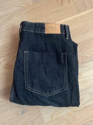 Mörkblå utsvängda jeans från Gina Tricot - Säljer ett par mörkblå jeans från Gina Tricot med hög midja och utsvängda ben. Jeansen har synliga knappar framtill. Perfekta för en trendig och avslappnad look. Använda 2-3 gånger! 