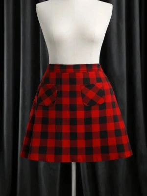 Röd och svart rutig kortkjol - A-linjeformad kortkjol i rött och svart rutigt mönster. Kjolen har två dekorativa fickor framtill och en hög midja. Perfekt för dig som gillar en retroinspirerad stil.