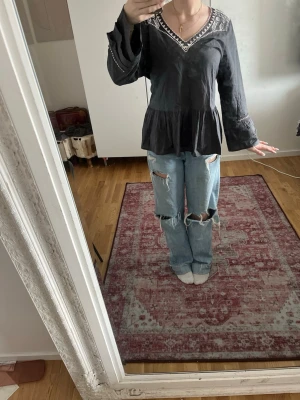 Svart blus med v-ringning och spetsdetaljer - Svart blus med v-ringning och dekorativa spetsdetaljer längs halsringningen. Blusen har långärmade, lätt utsvängda ärmar och en volang nedtill som ger en avslappnad siluett. Tillverkad i ett tunt, mjukt material som känns skönt mot huden. Pris kan diskuteras🩷