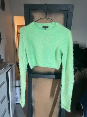Grön fluffig cropped tröja Current Mood - Säljer en neon grön, fluffig och cropped stickad tröja från Current Mood. Tröjan har långa ärmar, rund halsringning och är gjord i ett mjukt, lurvigt material som känns riktigt cozy. Perfekt för dig som vill sticka ut med en färgglad look.