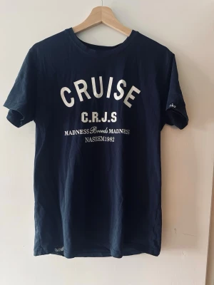 Marinblå CRUISE t-shirt med tryck - Snygg marinblå t-shirt från CRUISE med vit text och tryck både fram och bak. Klassisk rund hals och korta ärmar. Tillverkad i mjuk bomull, perfekt för en avslappnad och trendig stil.