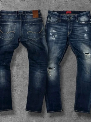 Mörkblå slitna jeans med detaljer - Säljer ett par mörkblå jeans med slitningar och distressed detaljer framtill. Jeansen har raka ben, klassiska fem fickor och kontrastsömmar. Skinnpatch bak i midjan och cool tvätt ger en trendig look.W30 L32