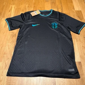 Brazil special jersey emerald - Snygg svart Brasilien fotbollströja från Nike med emerald detaljer på krage och ärmslut. Tröjan har korta ärmar, rund hals och Brasilien-emblemet på bröstet. Tillverkad i lätt och ventilerande material, perfekt för träning eller match.