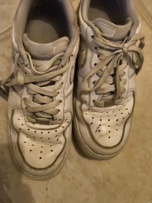 Vita Nike sneakers i skinn - Klassiska vita sneakers från Nike med perforerade detaljer på tån och sidorna. Skorna har en låg profil, rund tå och vita skosnören. Tillverkade i skinn med diskret Nike-logga på sidan och plös.