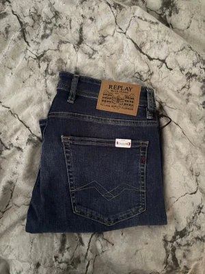 Mörkblå jeans replay  - Snygga mörkblå jeans från replay med raka ben och klassiska fem fickor. Jeansen har diskreta slitningar och kontrastsömmar, samt en läderpatch bak i midjan. Perfekta för en avslappnad och trendig look.
