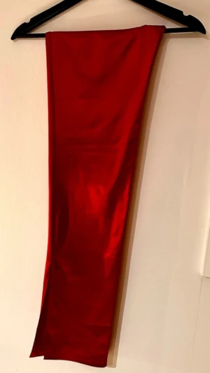 Röda satin byxor med slits  - Snygga röda byxor med utsvängda ben och slits nertill på sidan. Byxorna har en slät, figurnära passform och är tillverkade i ett stretchigt tyg som ger en bekväm känsla. Perfekta för dig som vill sticka ut med färg. Bredd - ca 32cm Innelängd - ca 81cm Längd - ca 113cm