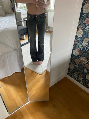 Svarta bootcut jeans med brodyr - Säljer ett par svarta bootcut jeans med snygg broderad ficka bak och kopparfärgad knapp. Jeansen har låg midja och klassisk femficksmodell. Perfekta för dig som gillar en avslappnad men ändå trendig stil.