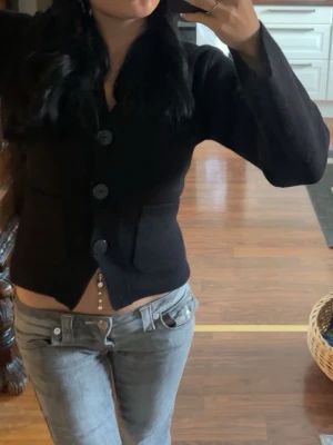 Svart kofta från Gina Tricot - Snygg svart kofta från Gina Tricot med stora knappar framtill och två fickor. Koftan har en croppad passform och är gjord i mjukt stickat material. Perfekt att slänga över en topp för en chill look. Storlek XS. Hund finns i hemmet därav finns det lite hår på den. Använd max 5 gånger. Inga anmärkningar