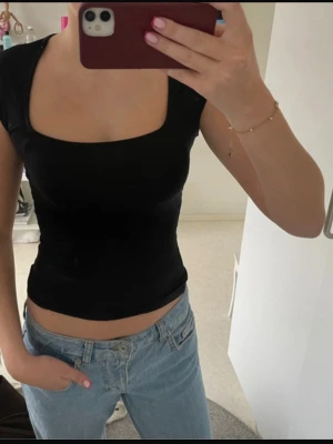 Kortärmad topp - Snygg svart croppad topp med fyrkantig ringning och korta ärmar. Perfekt att styla med jeans eller kjol för en trendig look. Tunn och stretchig kvalitet som sitter tight och framhäver figuren.