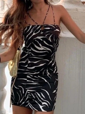 Svart zebramönstrad kort klänning - Trendig svart kort klänning med zebramönster och tunna axelband som korsas framtill. Klänningen har en liten cut-out detalj vid bröstet och en tight passform som framhäver figuren. Perfekt för dig som gillar att sticka ut med coola mönster. Från Zara storlek S