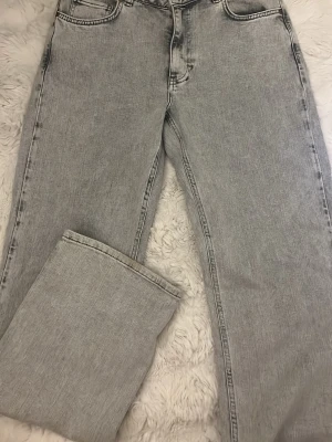 Grå mid wide jeans från bikbok  - Säljer ett par gråa jeans från bikbok med mid wide passform. Jeansen har klassisk femficksdesign, raka ben och normalhög midja. Materialet är denim i bomull och färgen är ljusgrå med tvättad look. Perfekta för en avslappnad och trendig stil.
