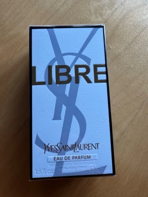 Yves Saint Laurent Libre Eau de Parfum - Säljer en elegant parfym från Yves Saint Laurent, Libre Eau de Parfum. Förpackningen är vit med stora bokstäver i guld och silver samt YSL-loggan. Flaskan innehåller 50 ml och är en påfyllningsbar spray. Perfekt för dig som gillar lyxiga dofter.