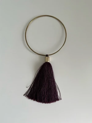 Gardintofs från Indiska i lila och guld - Elegant vinröd / lila gardinomtag / gardinspänne med härlig tofs och stilrent runt omtag i guld- / mässingsfärg. Klassisk och minimalistisk tassel-design som både håller ihop gardinen och ger en fin extra dekoration. Mycket gott skick!  (Skickas helst, men kan även hämtas i Stockholm vid behov)