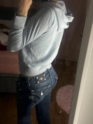 Mörkblå Miss Me jeans med detaljer - Säljer ett par mörkblå jeans från Miss Me med snygga silverfärgade knappar och broderade fickor bak. Jeansen har låg midja och bootcut passform, samt coola detaljer och slitningar som ger en trendig look.