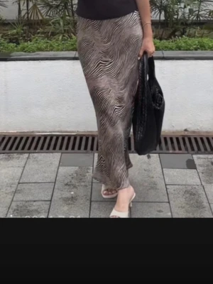 Zebramönstrad långkjol i satinlook - Snygg långkjol med zebramönster i beige och svart. Kjolen har en figurnära passform och ett mjukt, glansigt material som ger en lyxig känsla. Perfekt att styla med crop tops eller enkla linnen för en trendig look.