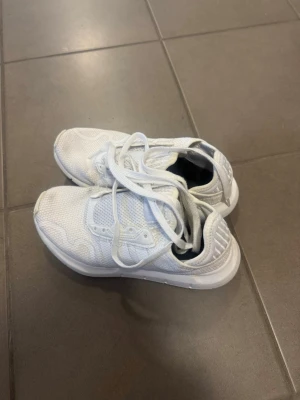 Vita Adidas sneakers i mesh - Snygga helvita sneakers från Adidas med klassiska tre ränder på sidan. Skorna är låga och har ovandel i mesh för bra ventilation och komfort. Perfekta för dig som gillar stilrena och sportiga skor. Skosnören i vitt och diskret Adidas-logga på plösen.