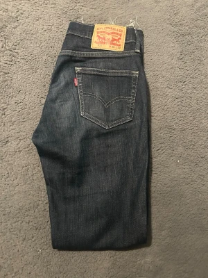 Levi's 511 mörkblå jeans W30 L32 - Mörkblå jeans från Levi's modell 511 med klassisk femficksdesign och kontrastsömmar. Jeansen har en smal passform och är tillverkade i denim med en snygg tvätt. Perfekta för en stilren och avslappnad look.