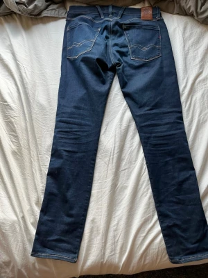 Mörkblå jeans från Replay jeans - Snygga mörkblå jeans från Replay Jeans med klassisk femficksdesign och raka ben. Jeansen har kontrastsömmar och läderpatch bak i midjan. Tillverkade i slitstark denim som ger en tidlös look.