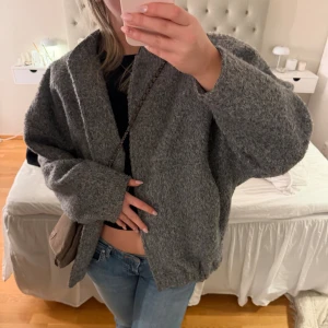 Grå oversized ulljacka - Mysig och oversized grå jacka i ullmix med lång ärm och enkel design. Jackan har en avslappnad passform och stängs framtill med dragkedja. Perfekt för lager på lager och en chill look. Storlek M/L
