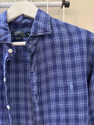 Blårutig skjorta från Polo Ralph Lauren - Snygg blårutig skjorta från Polo Ralph Lauren i slim fit. Skjortan har klassisk krage, vita knappar och det ikoniska broderade logotypen på bröstet. Perfekt för en avslappnad men stilren look.