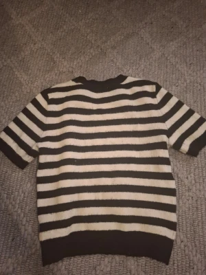 Svartvit randig stickad tröja - Kortärmad stickad tröja med breda svarta och vita horisontella ränder. Tröjan har rund halsringning och ribbade kanter vid ärmslut och nederkant. Materialet ser mjukt och bekvämt ut, perfekt för en avslappnad stil. Pris kan diskuteras❤️