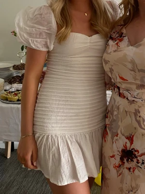 Vit kort klänning med puffärm - Supersöt vit kort klänning med puffärmar, smockad överdel och öppen rygg. Använd en gång.