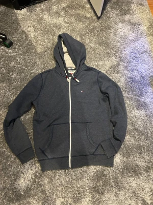 Tommy Hilfiger zip - Mörkblå zip hoodie med dragkedja från Hilfiger Denim. Klassisk modell med vit dragkedja, två fickor fram och justerbar huva med vita snören och färgdetaljer. Liten logga på bröstet och mjukt material på insidan för extra komfort. 