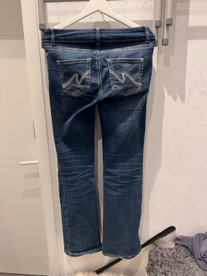 Blå bootcut jeans från Nelly - Säljer ett par blå bootcut jeans med snygga broderade detaljer på bakfickorna. Jeansen har klassisk femficksmodell, låg midja och är tillverkade i denim med lätt stretch. Perfekta för en avslappnad och trendig look. Ny pris är 500kr. 💛(Måt på sista bilden) 
