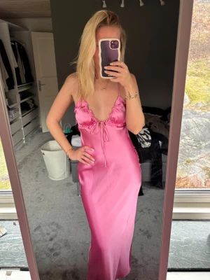 Rosa långklänning - Säljer en  rosa långklänning i satinliknande material med smala axelband, volangdetaljer och knyt framtill. Prislapp kvar 