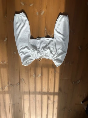 Sommar topp från Nelly  - Trendig vit topp med långa puffärmar och snörning framtill i midjan. Toppen har en lätt struktur i tyget och är perfekt för dig som vill ha en stilren men ändå unik look. 