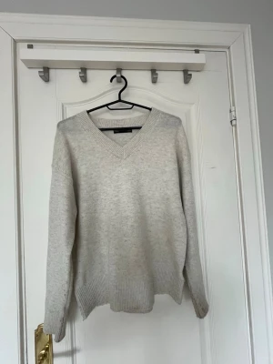 Ljusgrå stickad tröja från M&S - Ljusgrå stickad tröja från M&S Collection med v-ringad hals och ribbade muddar vid ärmslut och nederkant. Tröjan har en avslappnad passform och är perfekt för lager på lager. Tillverkad i mjukt material som känns skönt mot huden.