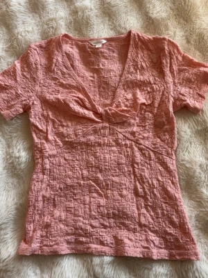 Rosa omlottopp från Dobber - Säljer en rosa topp från Dobber i storlek XS. Toppen har ett omlott och twistat parti vid bysten, korta ärmar och ett strukturerat material med diskret mönster. Perfekt för dig som gillar en feminin och trendig stil. Inga difekter, som ny!🩷