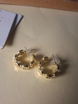 Guldpläterade chunky hoops örhängen - Snygga chunky hoops i guldpläterad metall med en unik länkdesign. Örhängena har rundad form och stängs med klassisk stift och plastplupp. Perfekta för dig som gillar trendiga accessoarer med lite extra attityd.