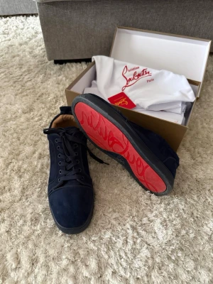 Mörkblå sneakers från Christian Louboutin - Snygga mörkblå sneakers från Christian Louboutin med klassisk röd sula. Skorna har en stilren design i mocka och läderdetaljer, samt svarta skosnören. Perfekta för dig som vill sticka ut med exklusiva detaljer.