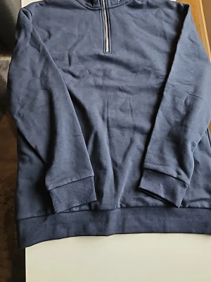 Mörkblå halfzip hoodie från 157 - Mörkblå hoodie från 157 med halv dragkedja framtill. Klassisk modell med ribbade muddar vid ärmslut och nederkant. Tillverkad i mjukt sweatshirtmaterial som är skönt att bära. Perfekt för en avslappnad och stilren look.