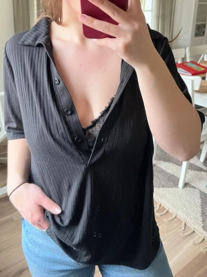 Svart ribbad tröja - Säljer en svart henley-skjorta, ribbad med korta ärmar. Skjortan har en djup v-ringning med knappar framtill..