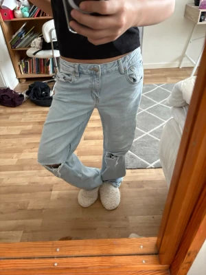 Ljusblå slitna jeans med hål - Ljusblå jeans med raka ben och slitna detaljer, inklusive hål på båda knäna. Klassisk femficksmodell med knapp- och dragkedjegylf. Perfekta för en avslappnad och trendig stil. Kommer ej till användning.