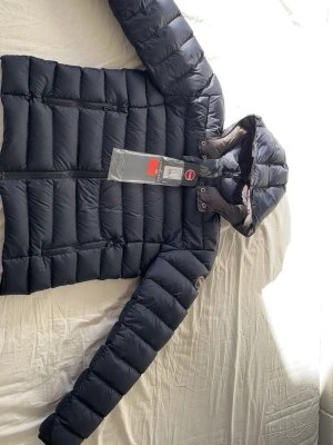 Colmar jacka - Snygg svart dunjacka från Colmar med huva och två dragkedjeförsedda fickor framtill. Jackan har quiltad design och diskret logotyp på ärmen. Perfekt för kalla vinterdagar och riktigt skön att bära. Materialet är glansigt och jackan har en modern, smal passform.