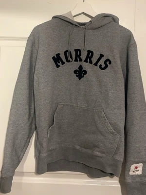Grå hoodie från Morris - Säljer en grå hoodie från Morris med mörkblå text och logga på bröstet. Hoodien har en klassisk känguruficka framtill, ribbade muddar vid ärmslut och nederkant samt en skön huva. Perfekt för chill dagar eller när du vill ha en enkel och snygg look. Storlek M men passar S också. Nypris: ca 1500 Mitt pris: 550. Skriv vid minsta lilla, priset går att diskutera!👍