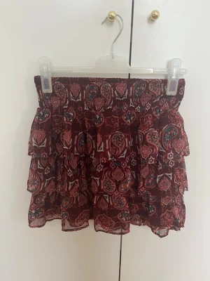 Mönstrad volangkjol från Lindex - Kort volangkjol från Lindex med vinrött mönster. Kjolen har resår i midjan och volanger